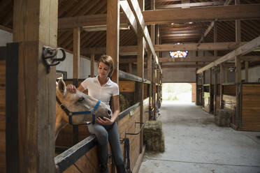 Kaukasisches Mädchen streichelt Pferd im Stall - BLEF06756