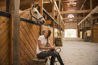 Kaukasisches Mädchen sitzt mit Pferd im Stall - BLEF06757