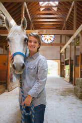 Kaukasisches Mädchen lächelnd mit Pferd im Stall - BLEF06765