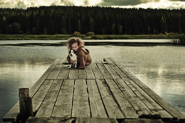 Kaukasisches Mädchen mit Hund auf Holzdeck in ruhigem See - BLEF06825