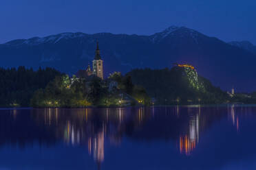 Dorfkirche und Gebäude spiegeln sich in einem stillen See bei Nacht, Bled, Oberkrain, Slowenien - MINF12310