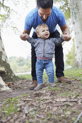 Kaukasischer Vater hilft seinem kleinen Sohn beim Laufen im Freien - BLEF06855