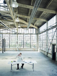 Caucasian businessman talking on cell phone in empty warehouse - BLEF06865