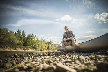 Older Caucasian man sitting in canoe on riverbed - BLEF06884