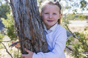 Lächelndes Mädchen, das einen Baum umarmt - BLEF06908