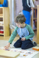 Junge ordnet Karten auf dem Boden im Klassenzimmer - BLEF06914