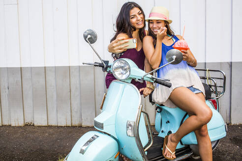 Pazifische Insulanerinnen fotografieren mit ihrem Handy auf einem Motorroller - BLEF07009