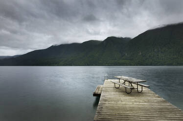 Picnic table on wooden pier at still remote lake - MINF12345