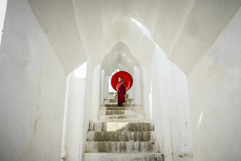 Asiatischer Mönch unter Schirm auf Tempeltreppe, Mingun, Mandala, Myanmar - MINF12354