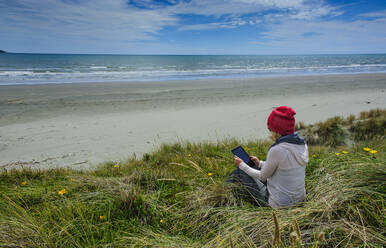 Frau mit Tablet am Strand von Foxton, Kapiti Coast, Nordinsel, Neuseeland - RUNF02688