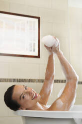 Caucasian woman taking bubble bath in bathroom - MINF12476