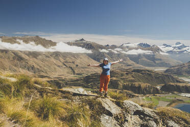 Frau steht mit ausgestreckten Armen auf dem Berggipfel, Roys Peak, Lake Wanaka, Neuseeland - IHF00130