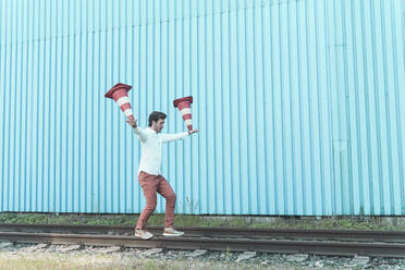 Young man balancing on rails, juggling traffic cones - UUF17831