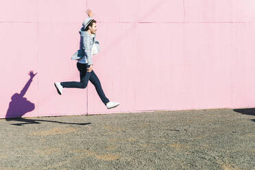 Young man in front of pink construction barrier, jumping in the air - UUF17833