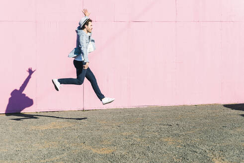 Junger Mann vor rosafarbenem Bauzaun, der in die Luft springt - UUF17833