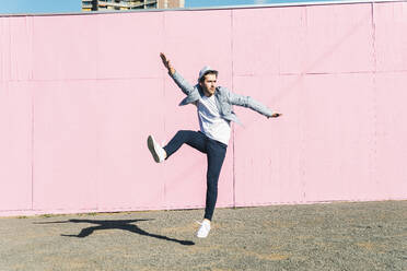 Young man in front of pink construction barrier, jumping in the air - UUF17834