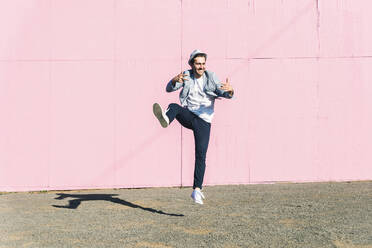 Junger Mann vor rosafarbenem Bauzaun, der in die Luft springt - UUF17836