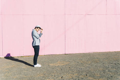 Young man in front of pink construction barrier, holding his hat - UUF17842