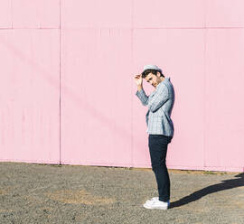 Young man in front of pink construction barrier, holding his hat - UUF17843