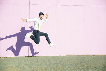 Young man in front of pink construction barrier, jumping in the air - UUF17847