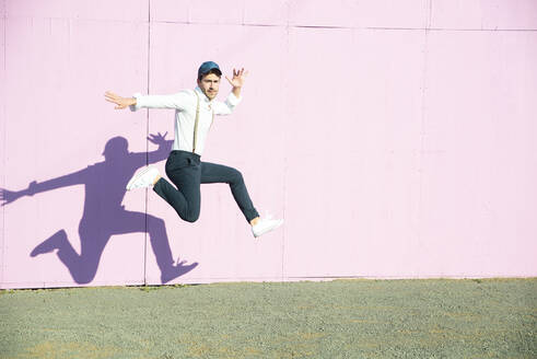 Junger Mann vor rosafarbenem Bauzaun, der in die Luft springt - UUF17847