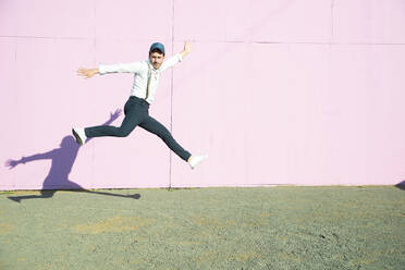 Junger Mann vor rosafarbenem Bauzaun, der in die Luft springt - UUF17848
