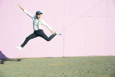 Junger Mann vor rosafarbenem Bauzaun, der in die Luft springt - UUF17852