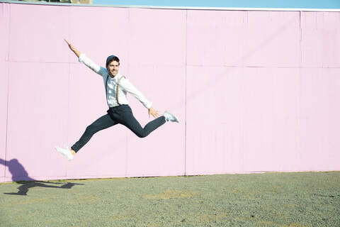 Young man in front of pink construction barrier, jumping in the air stock photo