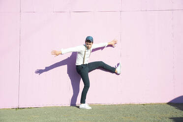 Young man in front of pink construction barrier, balancing on one leg - UUF17856