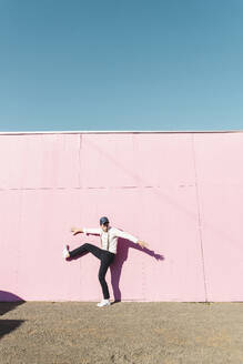 Junger Mann vor rosa Bauzaun, auf einem Bein balancierend - UUF17859