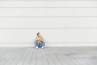 Young man wearing aloha shirt, sitting on ground, thinking - UUF17866