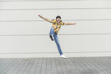 Young man wearing flat hat and aloha shirt, jumping for joy - UUF17867