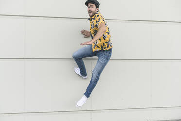 Young man wearing flat hat and aloha shirt, jumping for joy - UUF17869