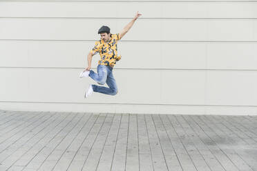 Young man wearing flat hat and aloha shirt, jumping for joy - UUF17876