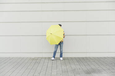 Junger Mann mit Aloha-Hemd, der einen gelben Regenschirm hält - UUF17879