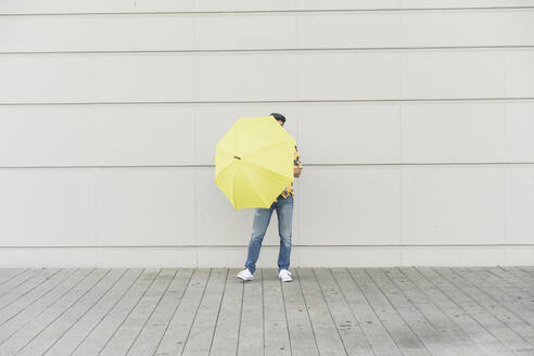 Junger Mann mit Aloha-Hemd, der einen gelben Regenschirm hält - UUF17879