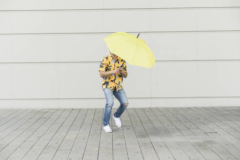 Junger Mann mit Aloha-Hemd, der einen gelben Regenschirm hält - UUF17880