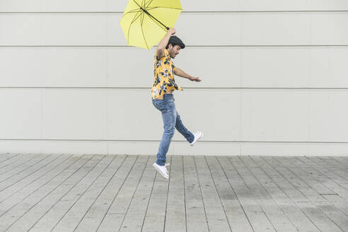 Junger Mann mit Aloha-Hemd, tanzend mit gelbem Regenschirm - UUF17881