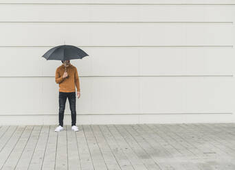 Junger Mann mit Regenschirm steht auf der Straße - UUF17885