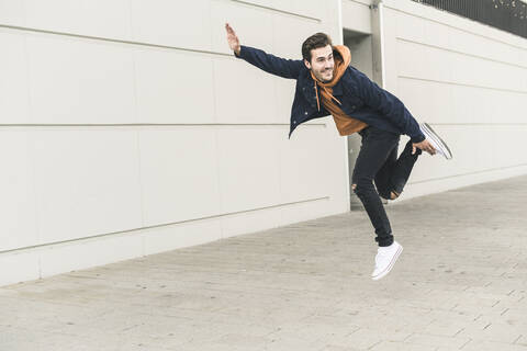 Junger Mann, der auf die Straße springt und so tut, als würde er fliegen, lizenzfreies Stockfoto