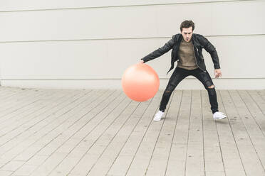 Young man in leather jacket, playing with a gym ball - UUF17891