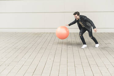 Young man in leather jacket, playing with a gym ball - UUF17893