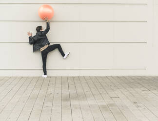 Young man in leather jacket, playing with a gym ball - UUF17896