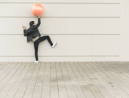 Junger Mann in Lederjacke, der mit einem Gymnastikball spielt - UUF17896