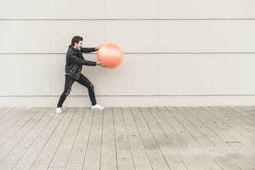 Young man in leather jacket, playing with a gym ball - UUF17897