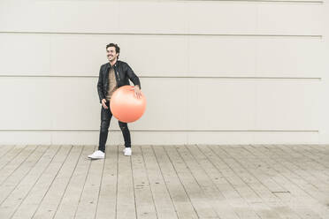 Young man in leather jacket, playing with a gym ball - UUF17899
