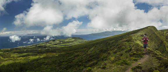 Hiker walking on hilltop dirt path over Cabeco Gordo crater, Faial, Portugal - MINF12556