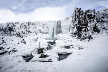 Waterfall pouring over icy cliffs in remote landscape - MINF12563