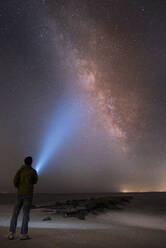 Asian man shining flashlight on starry sky - MINF12631