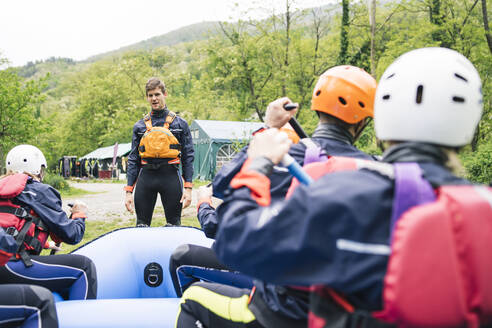 Kursleiter im Gespräch mit einer Gruppe von Freunden bei einem Raftingkurs - FBAF00728